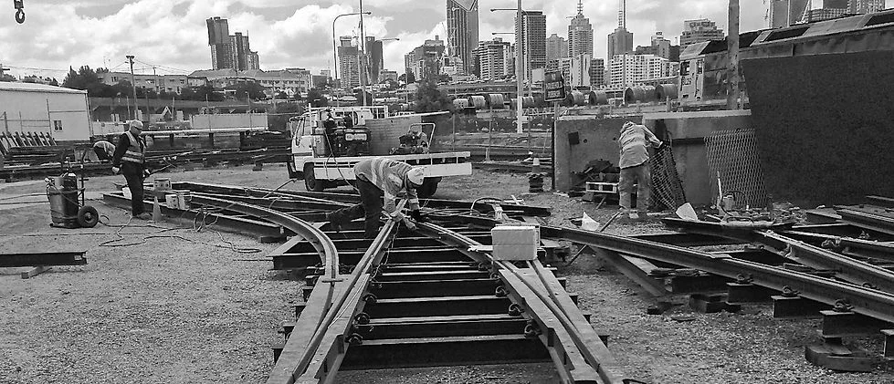 Crews working turnout components in a rail yard, with the Melbourne skyline behind.
